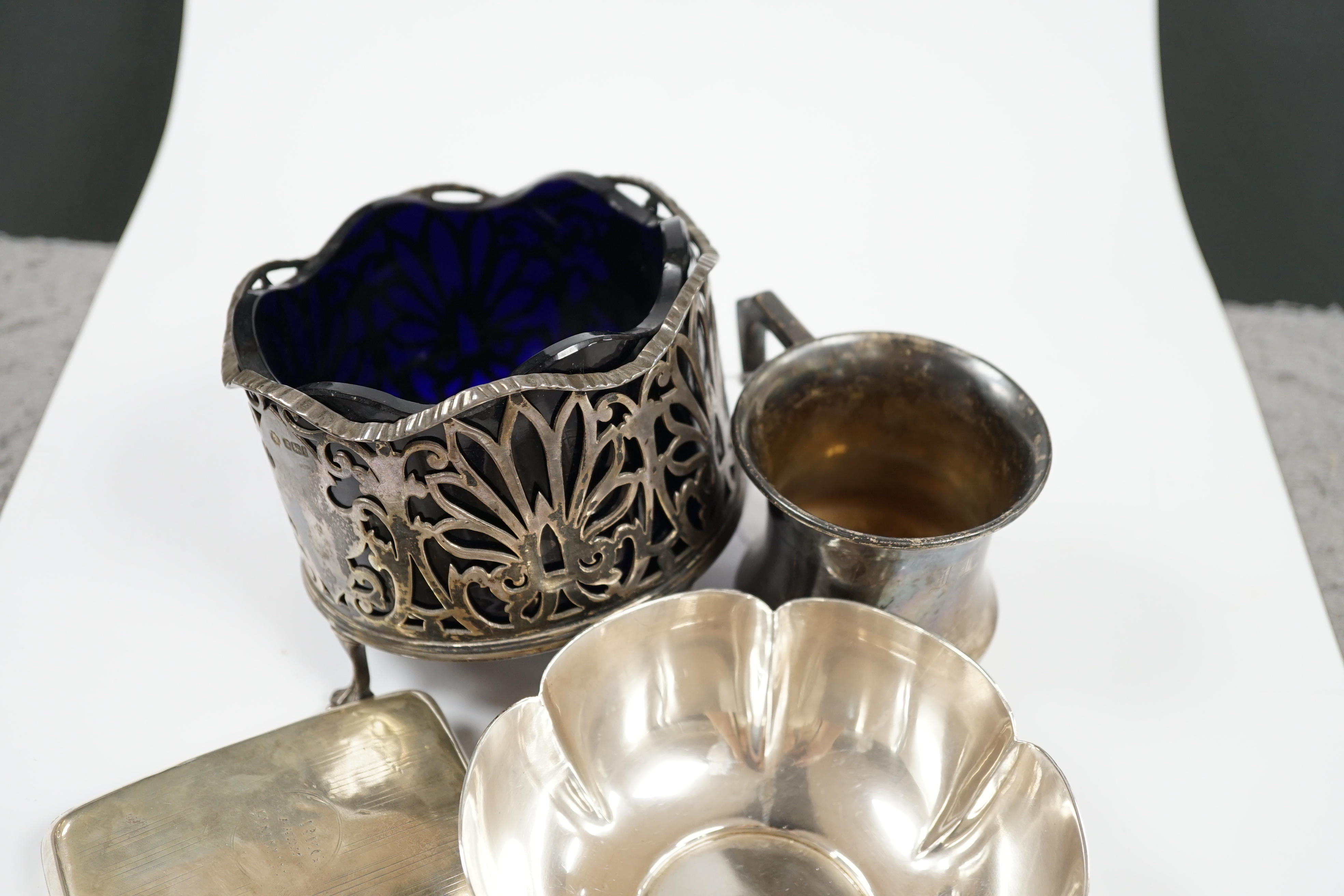 Sundry small silver including a modern bowl by G.J. Dennis, a napkin ring, cigarette case, christening mug and damaged bottle coaster with blue glass liner, together with three items of flatware including a Victorian Iri